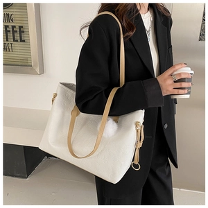 Close-up of white embossed tote bag featuring plush charm and brown shoulder straps