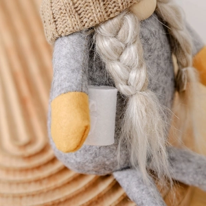 Handmade Christmas gnome plush with knitted heart hat and long white braids on wood background
