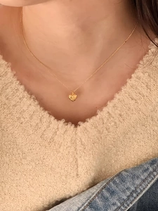 Close-up of a gold heart pendant necklace worn on a beige knit sweater and denim