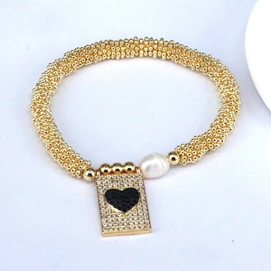 Macro detail of gold beaded bracelet with freshwater pearl and heart pendant charm