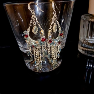 Detailed view of luxury gold tassel earrings with blue and red crystals hanging on glass