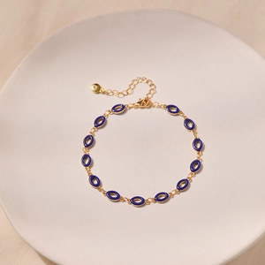 Detail of vintage golden chain bracelet with deep blue enamel oval charms on ceramic tray