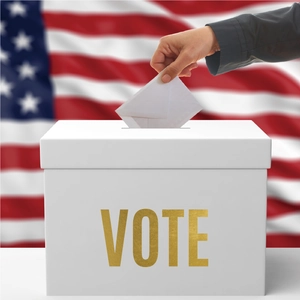 Detail of hand casting envelope into white ballot box with gold VOTE text and US flag