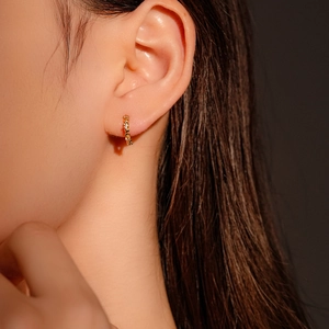 Close-up of golden geometric diamond-set hoop earring on model, high detail finish
