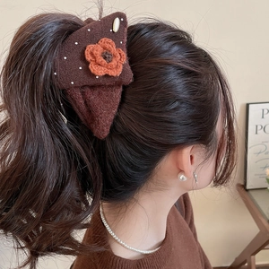 Detail of plush flower hair claw clip in dark brown knit fabric on model hair