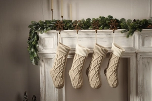 Detail of cream cable knit Christmas stockings hanging on a fireplace mantel