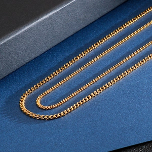 Detailed close-up of layered gold curb chain necklaces on a textured dark blue surface