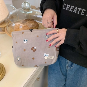 Grey linen makeup pouch featuring cute cat embroidery and zipper, held by a model