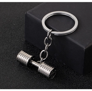 Macro shot of silver dumbbell keychain on black leather background for fitness lovers