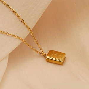 Macro shot of gold 18K titanium book necklace pendant with Bible and cross engraving