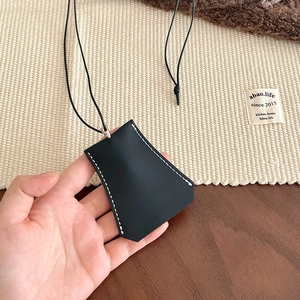 Close-up of black leather clochette key case with white contrast stitching and cord
