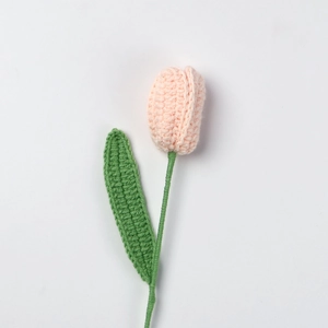 Detail der rosa handgestrickten Tulpenblüte mit grünem Stiel aus Häkelbaumwollgarn