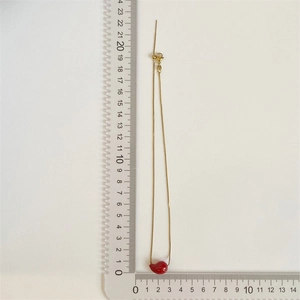 Detailed measurement of gold necklace with red teardrop pendant on a scale ruler