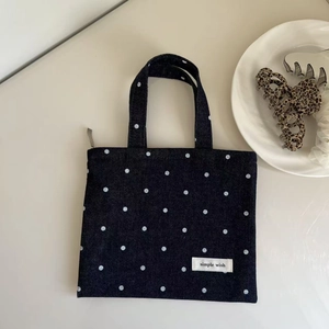 Detailed top view of a dark blue denim polka dot handbag with a simple wish woven label