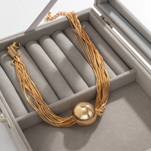Detailed view of layered gold chain necklace with sphere pendant in a velvet box