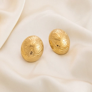 Macro view of gold stainless steel oval earrings with spiral texture and feather engraving