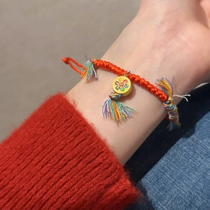 Vue détaillée du bracelet en corde rouge tressée avec pendentif doré et pompon coloré