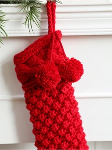 Close-up of red chunky knit Christmas stocking with two decorative pom poms on a mantel
