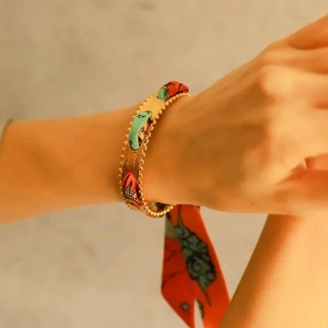 Detail of matte gold cuff bracelet with orange and green printed silk scarf woven through