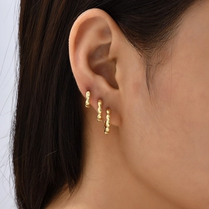 Macro detail of three graduated gold beaded hoop earrings worn on an earlobe