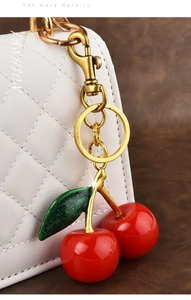 Close-up of red cherry resin pendant on white leather bag with golden keychain