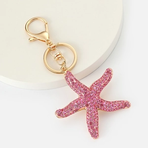Detailed macro view of a pink rhinestone starfish keychain with a golden clasp on white surface