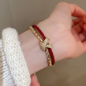 Détail d'un bracelet en cuir rouge et chaîne dorée avec un charm en croix serti de cristaux