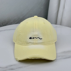 Pale yellow distressed baseball cap with embroidered letters and torn brim details