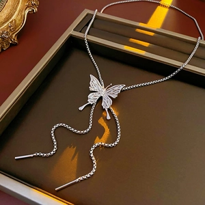 Close-up of a silver butterfly pendant necklace placed on a metallic tray with warm lighting