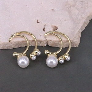 Detail view of gold C-shaped earrings with round white pearls on a pink stone background