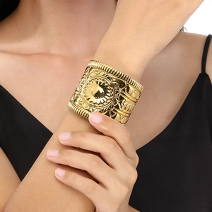 Detailed close-up of wide golden cuff bracelet with intricate ethnic sunburst engraving