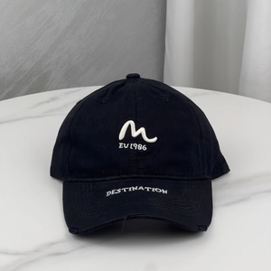 Detailed close-up of embroidered M-logo and EV 1986 text on a black cotton baseball cap