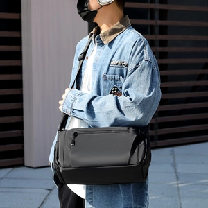 Waterproof black crossbody messenger bag for men, shown on shoulder in outdoor urban setting