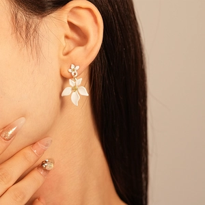 Détail de boucles d'oreilles florales blanches superposées portées par un mannequin