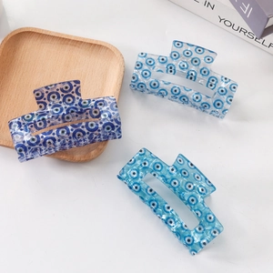Three rectangular blue evil eye pattern hair claws set on a white desktop with props