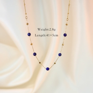 Close-up of gold stainless steel necklace with blue stone beads on white fabric