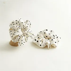 Detail view of two cream velvet hair scrunchies with black polka dots on a wooden stand