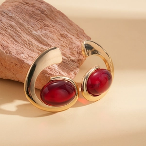 Irregular oval red resin earrings in golden metal finish on minimalist stone background