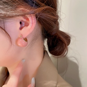 Close-up of a pink bead hoop earring worn on an ear showing the glossy gold-plated metal clasp