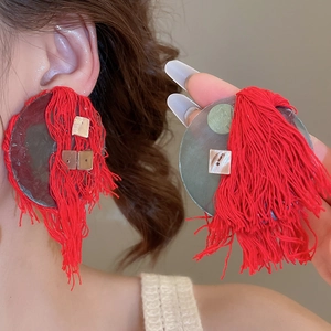 Close-up of a large red fringe earring with shell and metal details on model