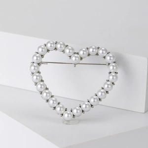 Detail view of heart-shaped hollow brooch with white pearls on a silver metal frame
