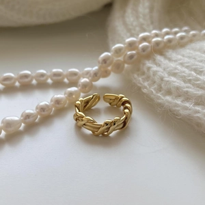 Detail of a golden twisted rope open ring placed on soft white knit fabric with pearls