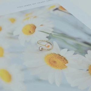 Adjustable golden twist ring with fresh water pearls on a floral card background
