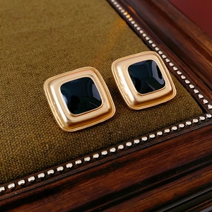 Macro detail of vintage gold square earrings with black enamel on green velvet cushion