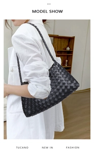 Side view of black hand-woven leather tote bag paired with white blazer on model