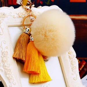 Close-up of beige plush pompom and yellow gradient silk tassels on gold keychain