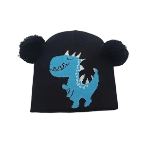 Dettaglio del cappello in maglia per bambini con due pompon e motivo dinosauro blu