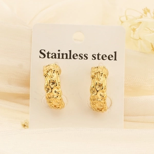 Detail of gold C-shaped earrings with irregular lava texture on white silk fabric