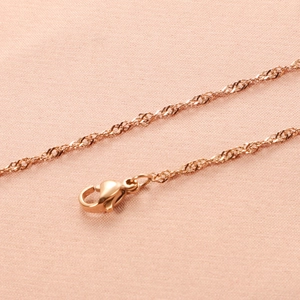 Detailopname van roségouden watergolfketting met karabijnsluiting op roze stof
