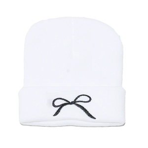 Close-up of white knitted beanie featuring detailed black bow embroidery on the fold